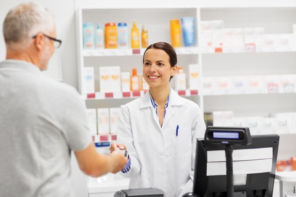 A Female Pharmacist Is Shaking Hands With A Man In A Pharmacy — Coastal Registers & POS In Murwillumbah, NSW