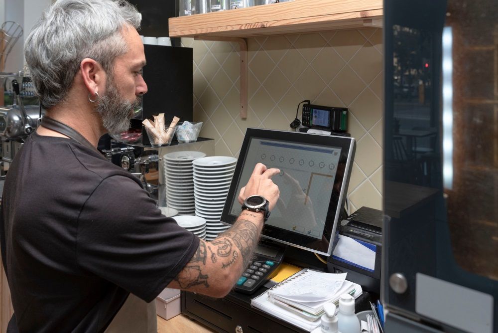 A Man Is Using A Computer In A Restaurant — Coastal Registers & POS In Ruthven, NSW