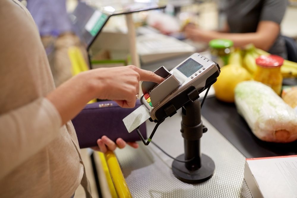 A Woman Is Using A Credit Card Machine In A Grocery Store — Coastal Registers & POS In Ruthven, NSW
