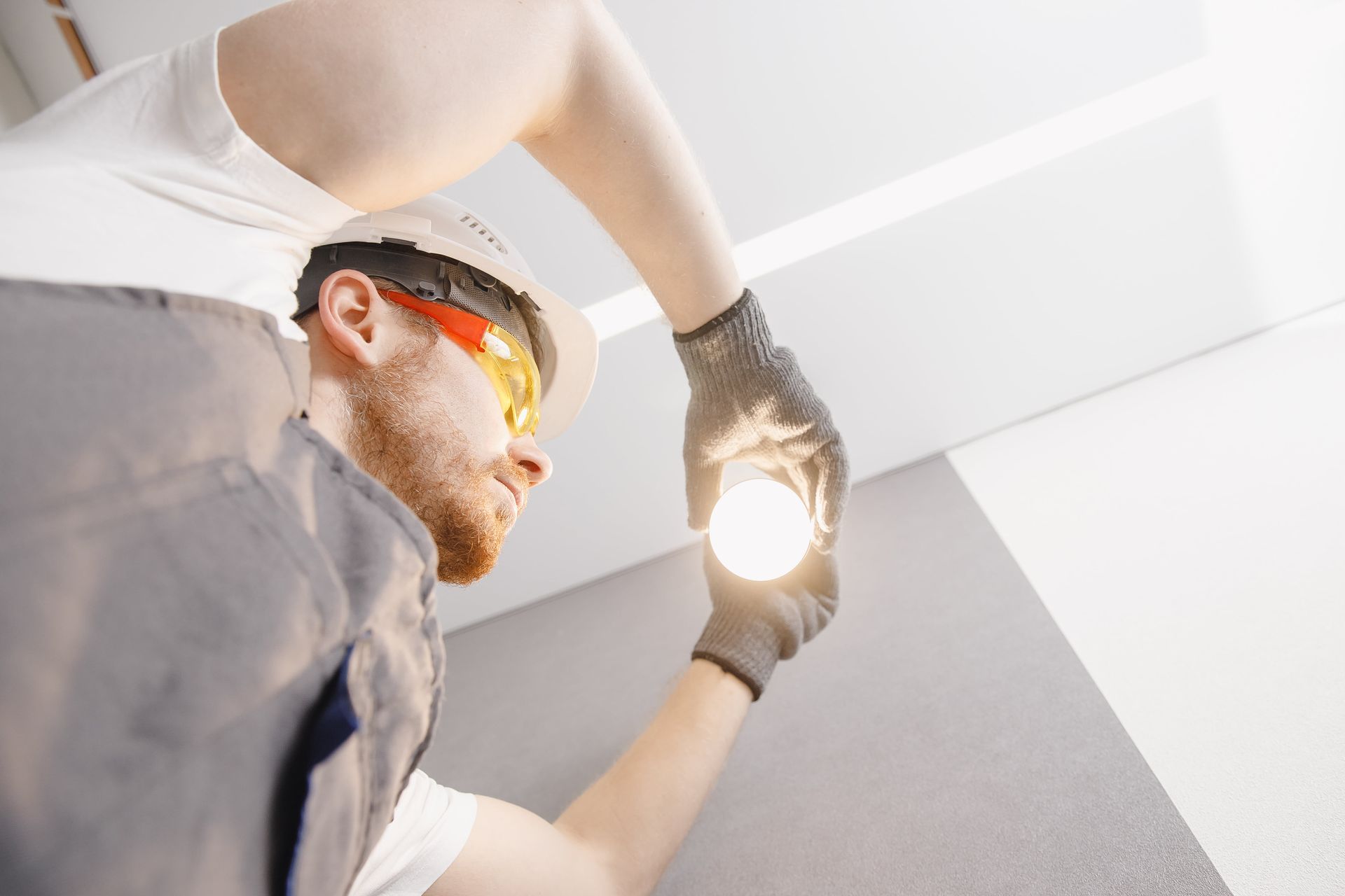 Worker installing a ceiling light, wearing safety glasses and gloves