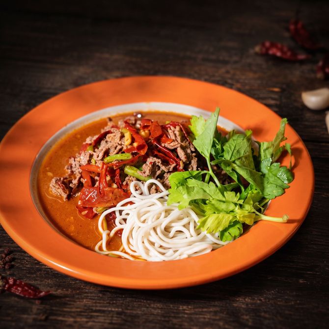 Orange plate of noodle soup topped with herbs and red chili on a dark table