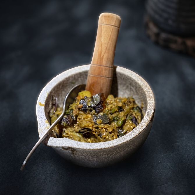 Stone mortar and pestle with green chutney and a spoon on a dark surface