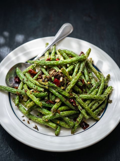 Roasted green beans with red pepper flakes on a white plate, with a spoon.