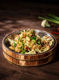 Rustic bowl of mixed vegetable salad topped with herbs and sesame seeds on a dark wooden table