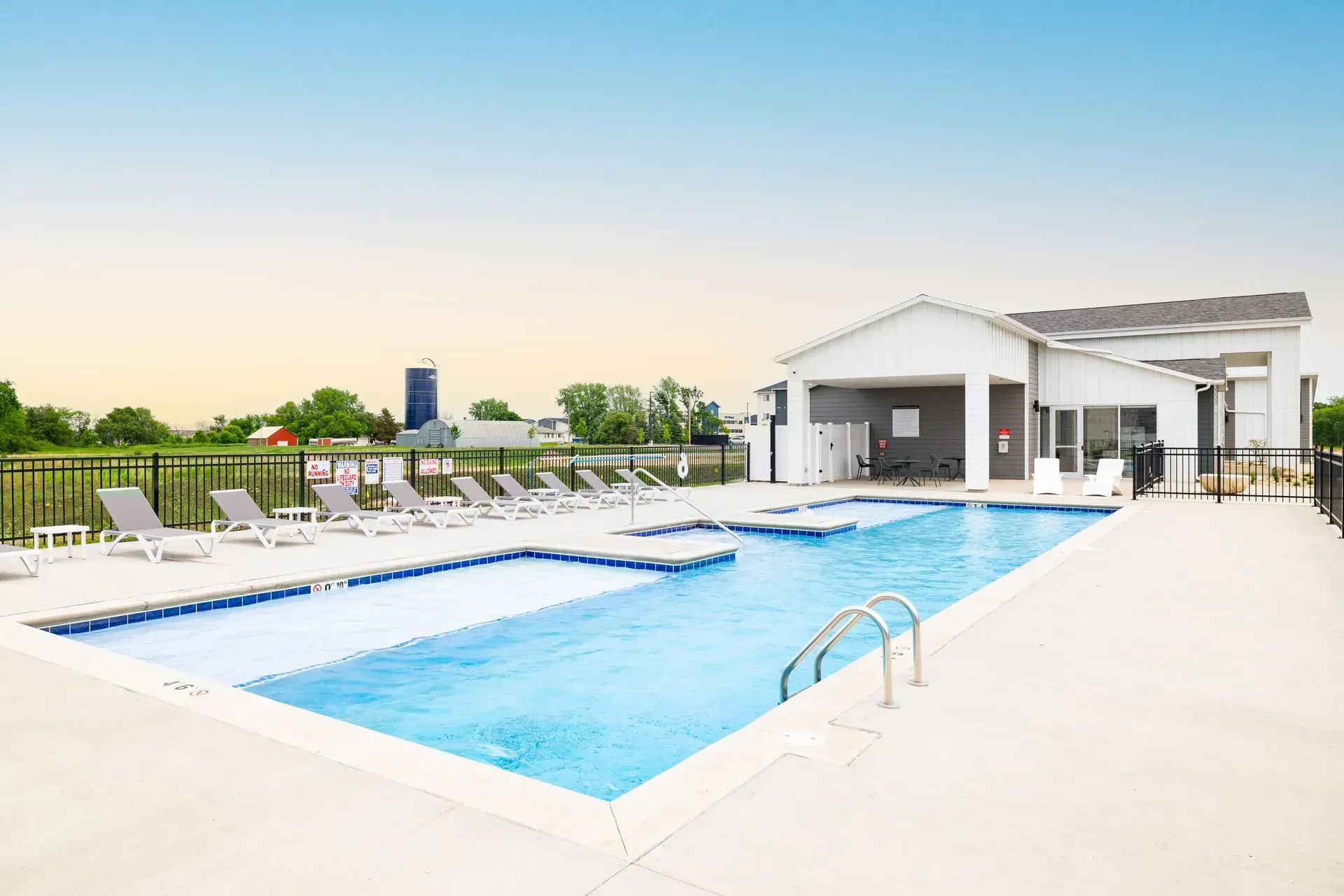 Outdoor rooftop pool with lounge chairs, clear blue water, and a white cabana at sunset