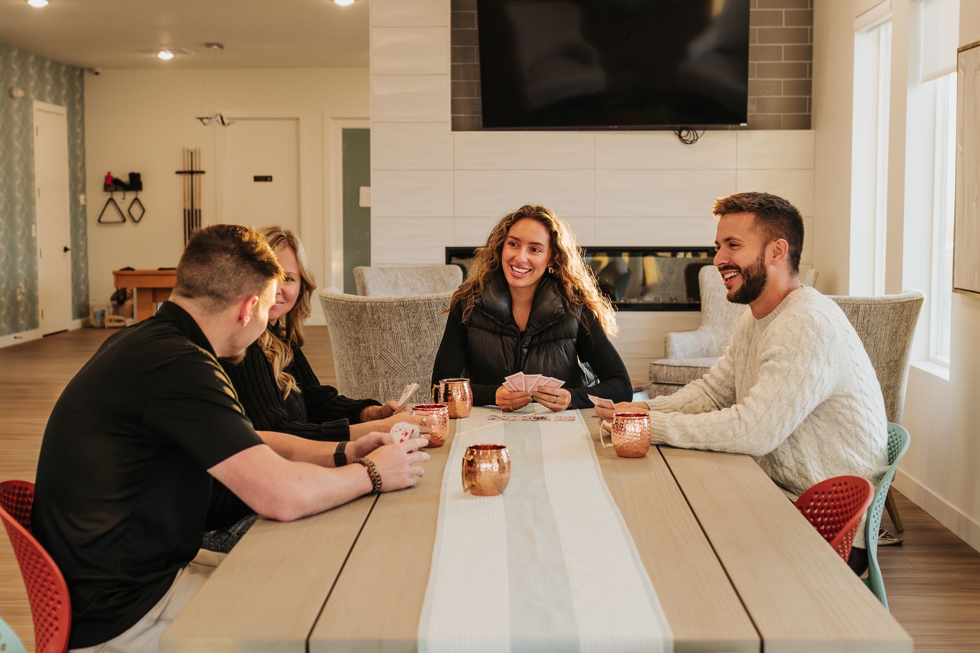 People chatting around a dining table in a bright living room, with a TV and fireplace in the background
