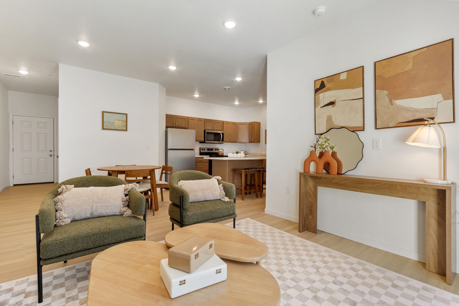 Bright open-plan living room with white chairs, coffee table, dining area, and kitchen island in the background