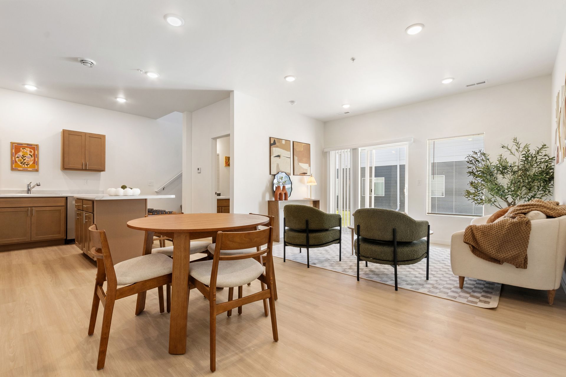 Bright white open-plan dining and kitchen area with wood floors and black chairs around a table.