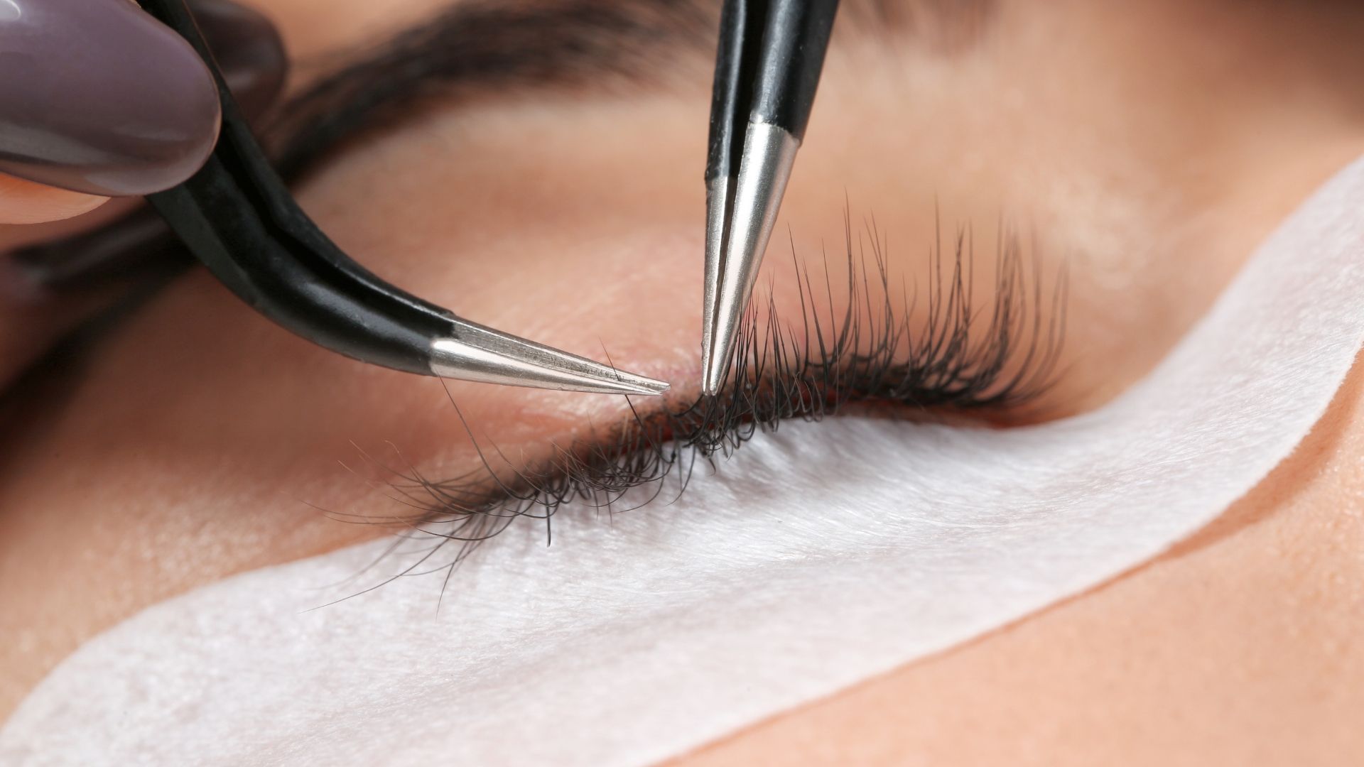 Close-up of eyelash extensions being applied with tweezers to a closed eye