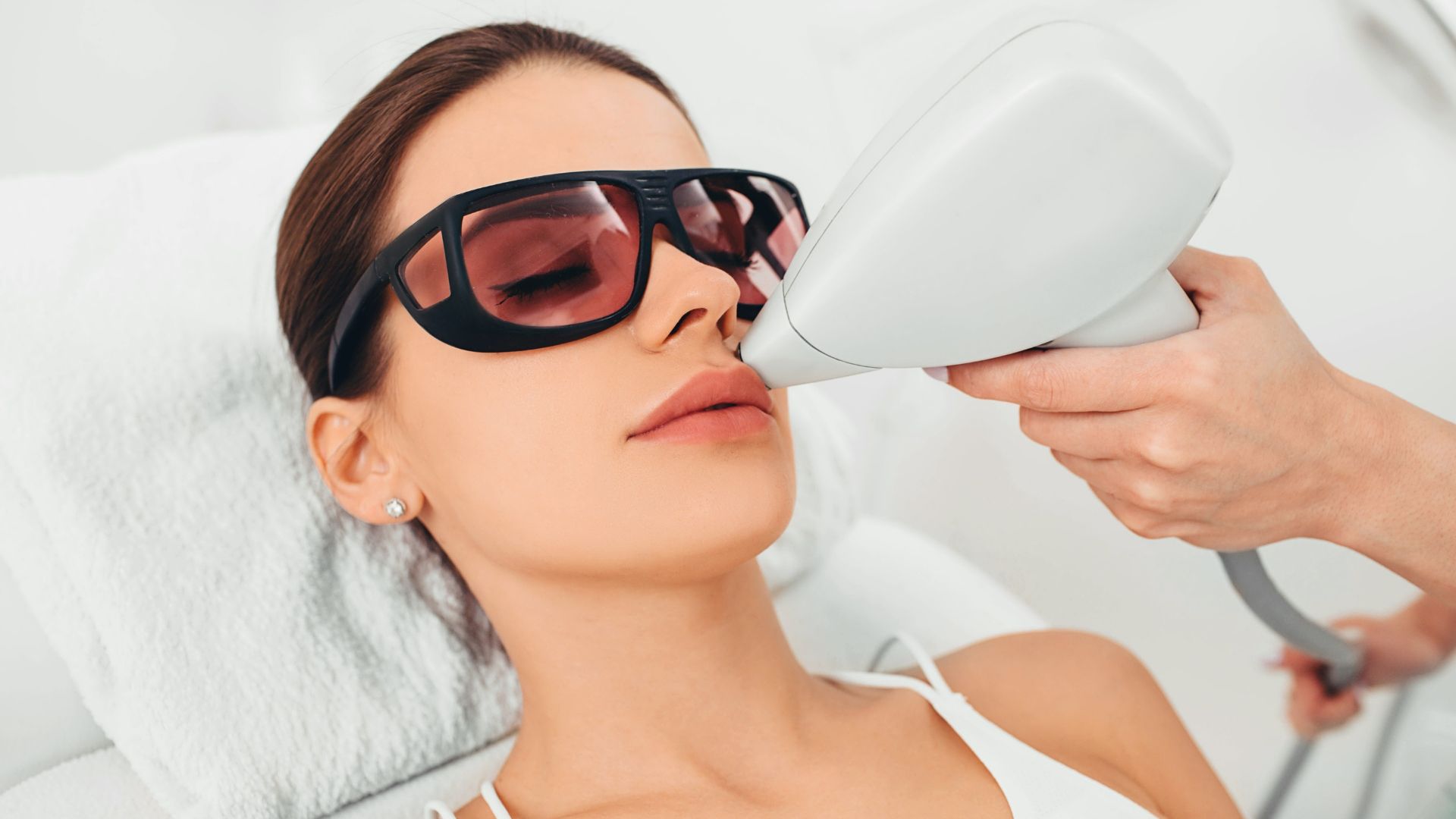Woman wearing dark goggles during a facial laser treatment in a clinic-like setting
