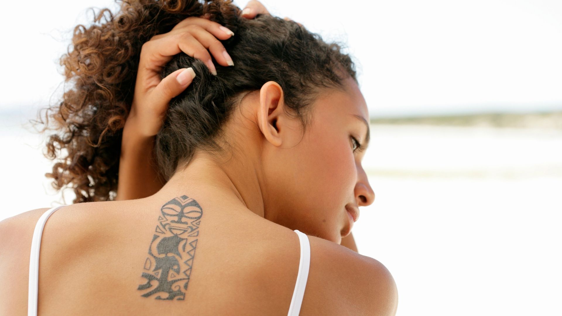Person scratching the back of their neck, showing a tattoo on the upper back.