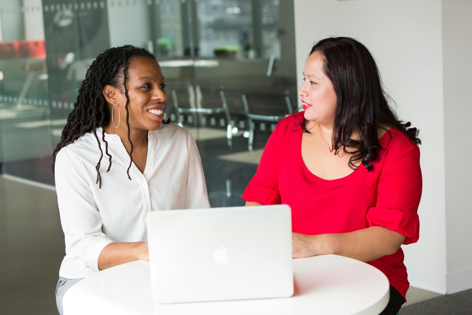Two women smiling and looking at a laptop computer. One in a white shirt, one in a red shirt.