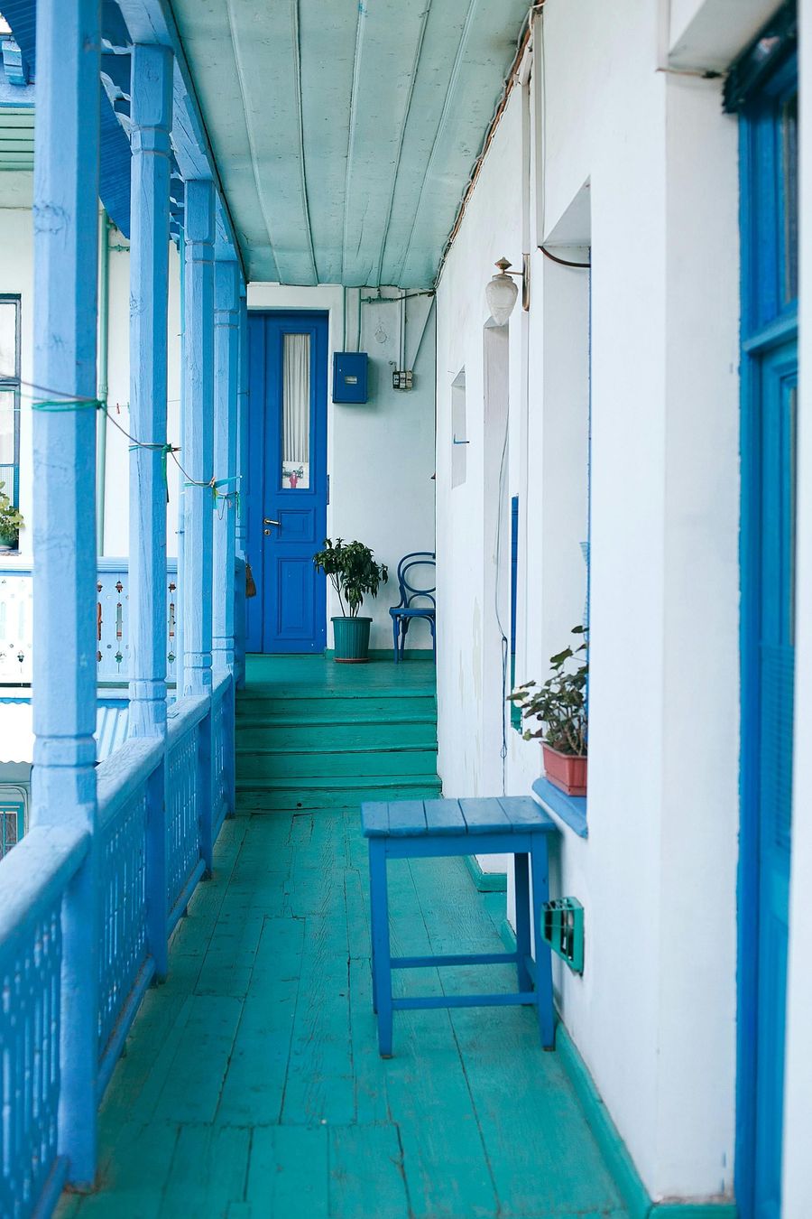 Blue balcony with matching door and stool, white building.