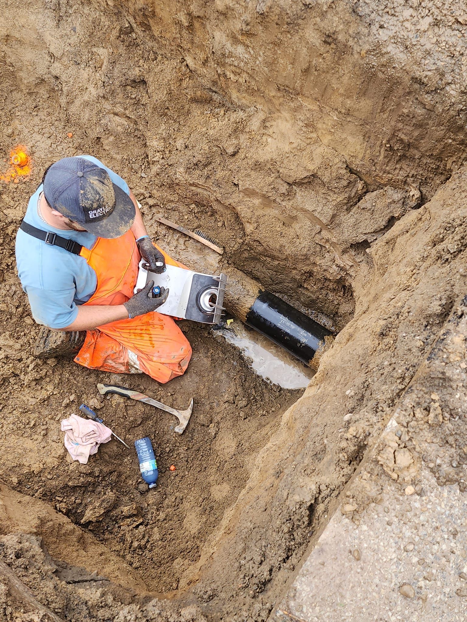 A man is kneeling in the dirt working on a pipe.