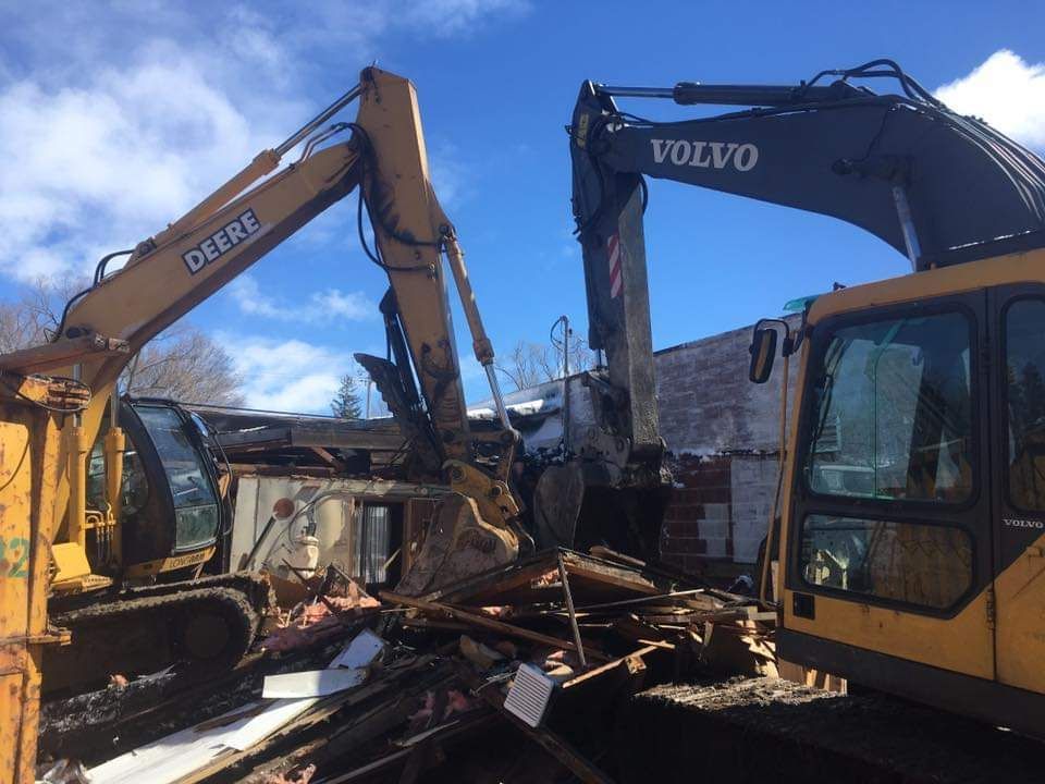 A deere excavator and a volvo excavator are demolishing a building