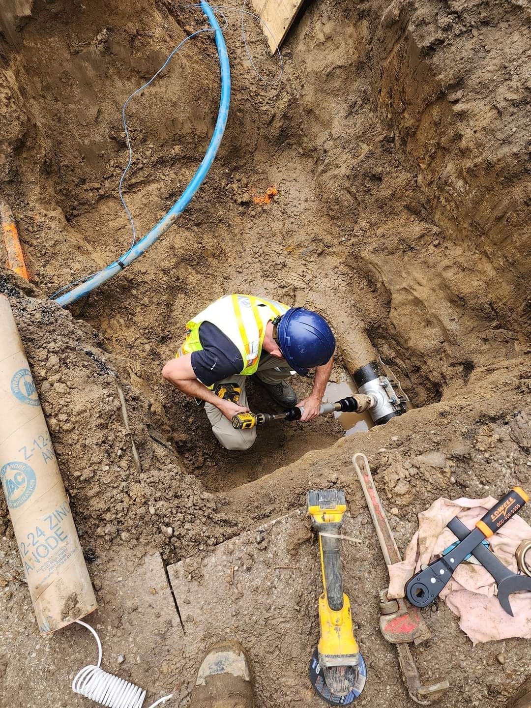 A man is working on a pipe in a hole in the ground.