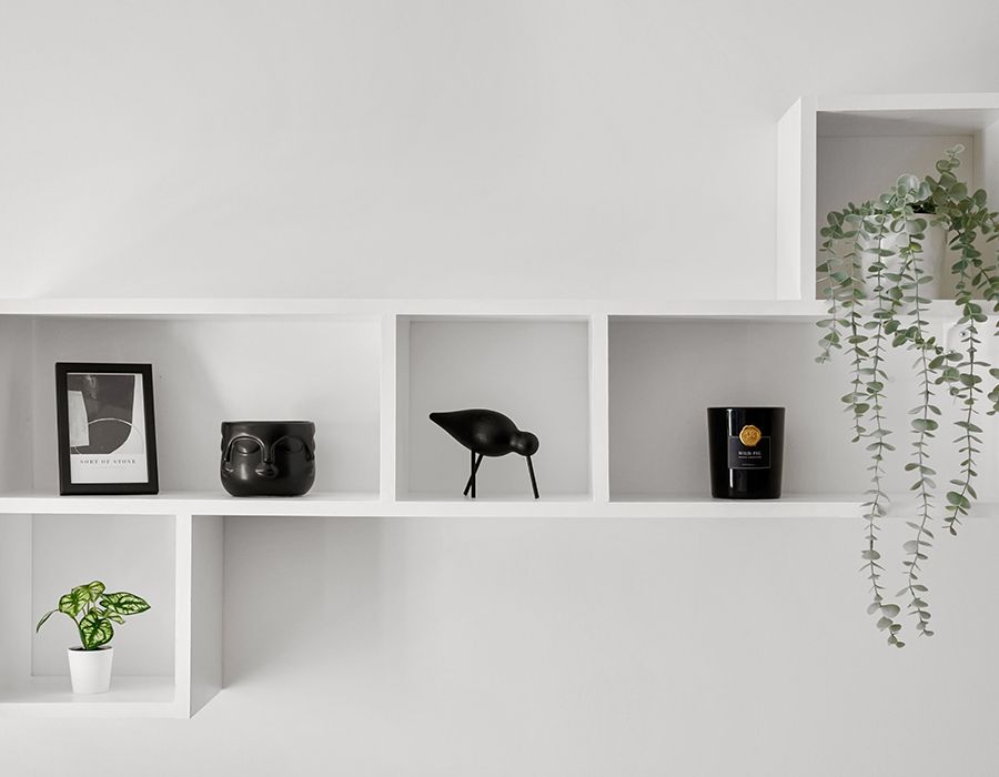 Minimal white wall shelves with small decor, plants, and a hanging vine in a bright room