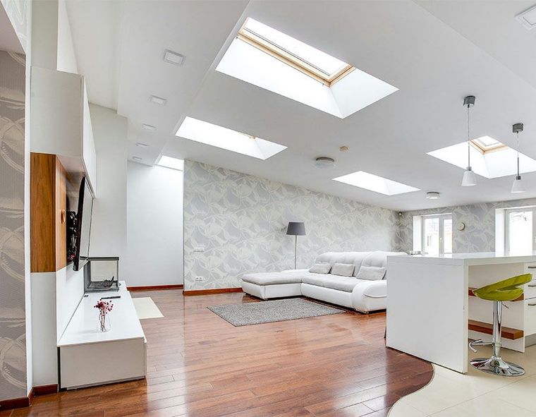 Bright modern living room with white sectional sofa, skylights, hardwood floors, and a bar stool island