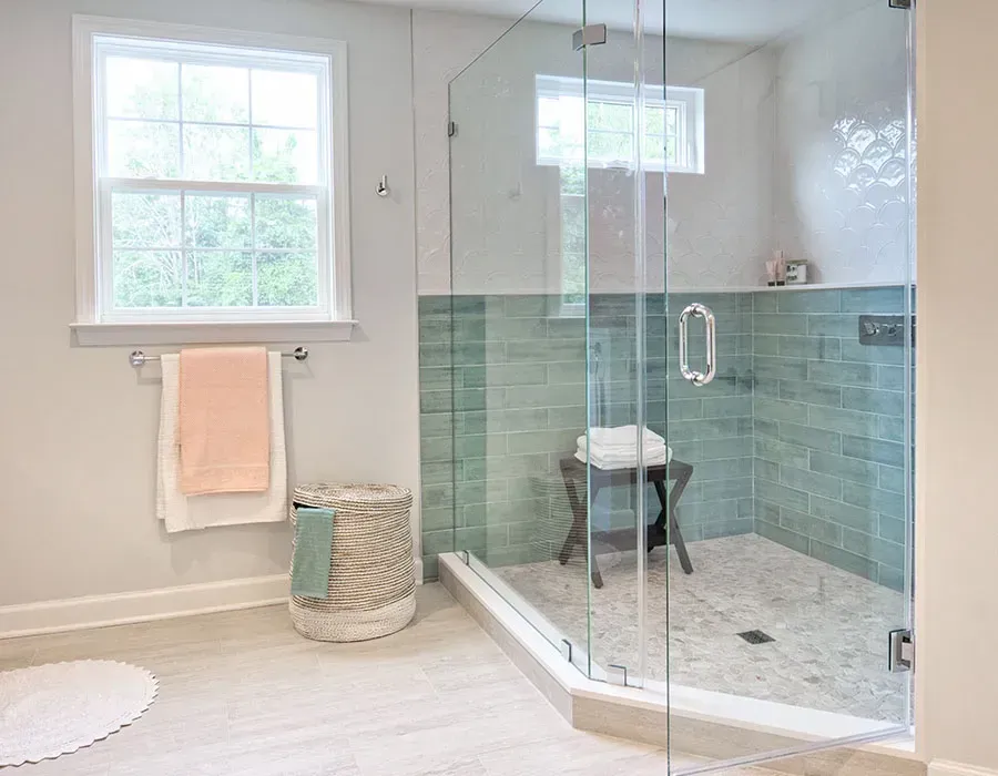 Bright modern bathroom with glass shower, pale blue tile, and window with towels hanging nearby
