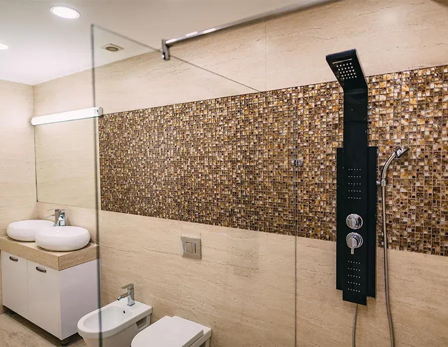 Modern bathroom with mosaic tile accent wall, sink, toilet, and black shower panel with overhead rain shower.