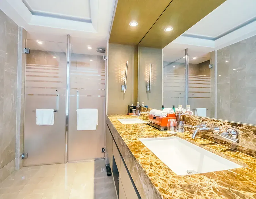 Modern bathroom with glass shower, marble vanity, double sinks, and gold-toned finishes