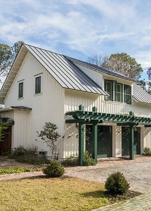 White farmhouse with green trim and pergola in a sunny yard