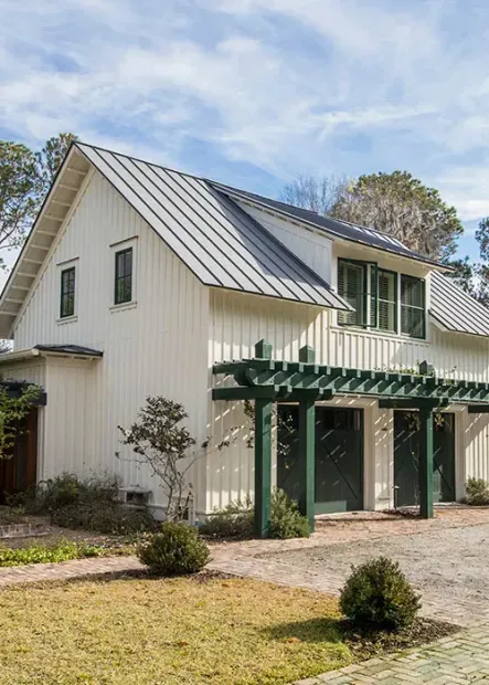 White farmhouse with green trim and pergola in a sunny yard