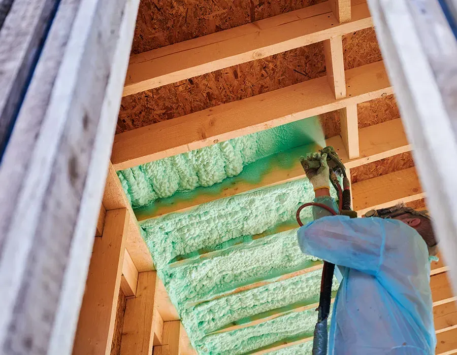 Worker spraying green foam insulation in an unfinished wooden ceiling cavity