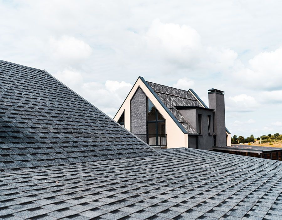 Rooftops with dark gray shingles and modern houses under a cloudy sky