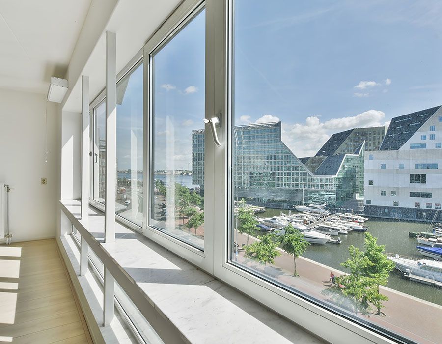 Bright hallway with large windows overlooking modern buildings and a marina under blue sky.