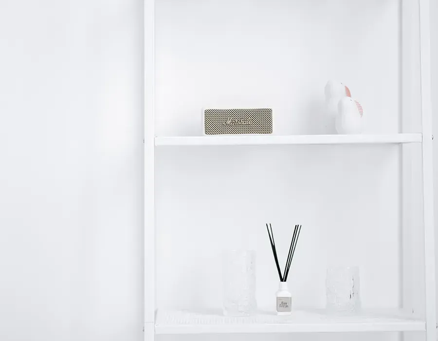 White shelf with a small patterned box, white decor, and a reed diffuser on a minimal wall niche.