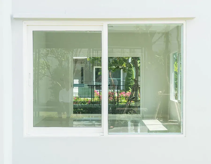 White-framed window overlooking a garden with trees and pink flowers outside