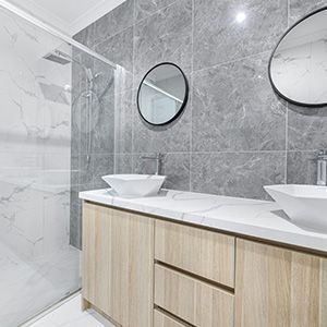 Modern bathroom with gray tile walls, glass shower, floating wood vanity, and round mirrors