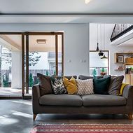 Modern living room with a dark sofa, colorful pillows, and open sliding doors to a bright patio.