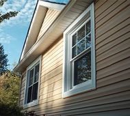 House exterior with tan siding and white-trimmed windows under a blue sky