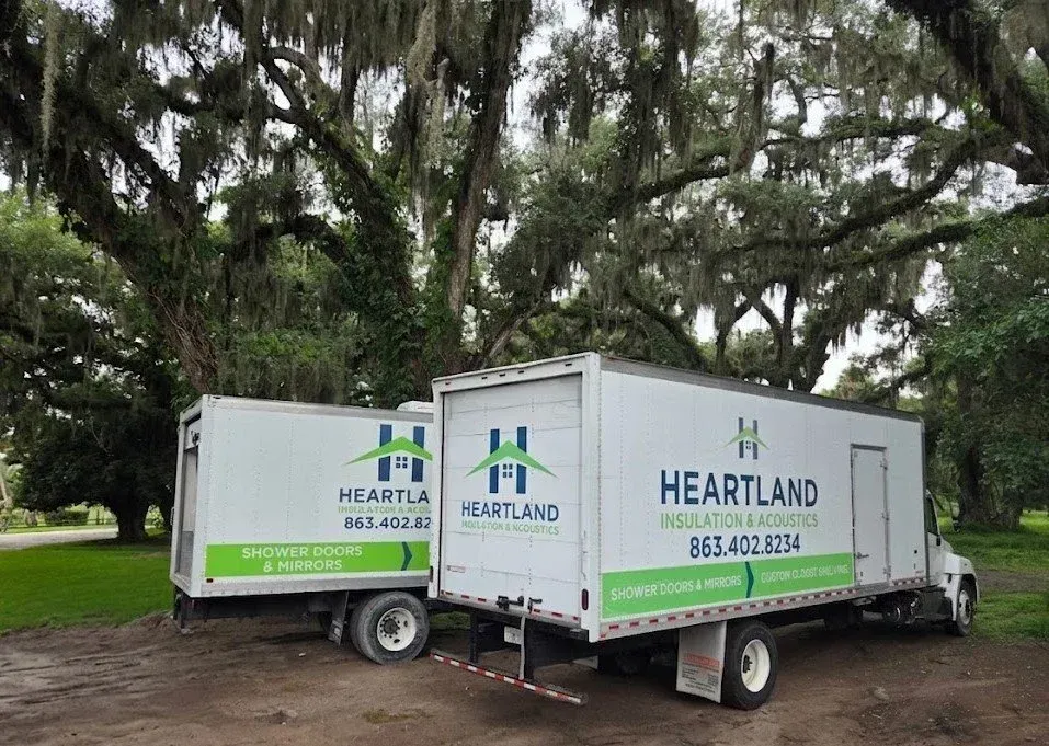 White Heartland trailer parked under trees with green logo and phone number.