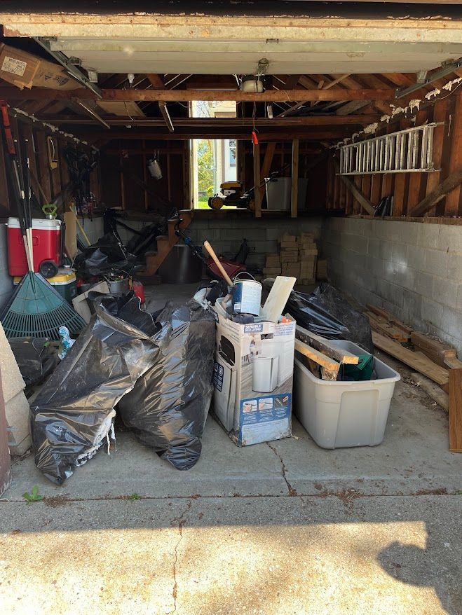 Messy garage filled with debris and garbage bags; open doorway in the distance.