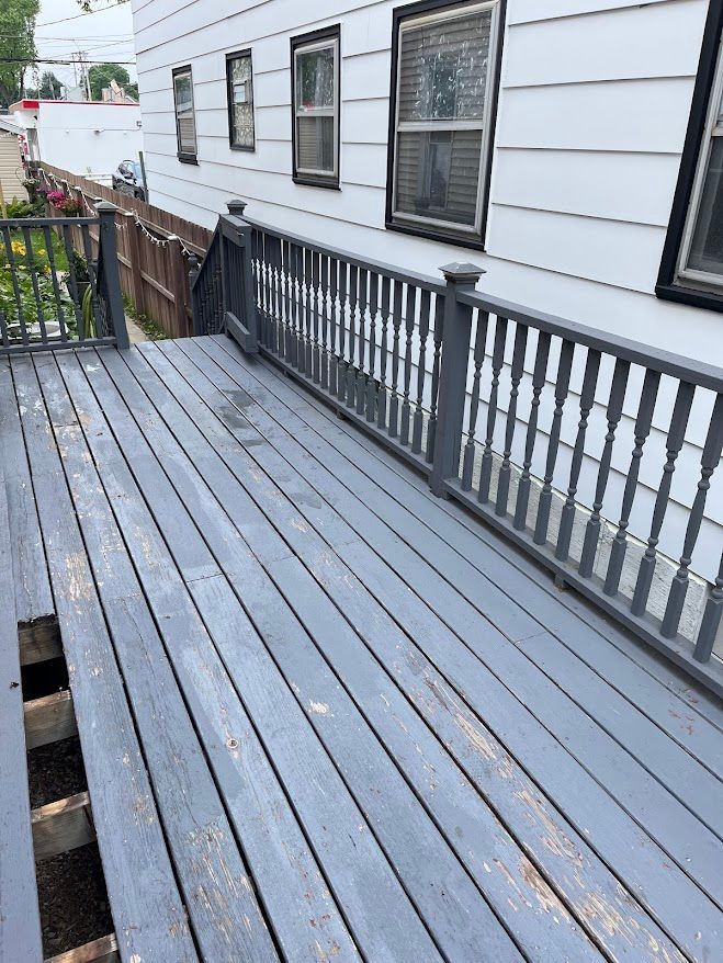 Gray wooden deck with peeling paint, railing, and a white building in the background.