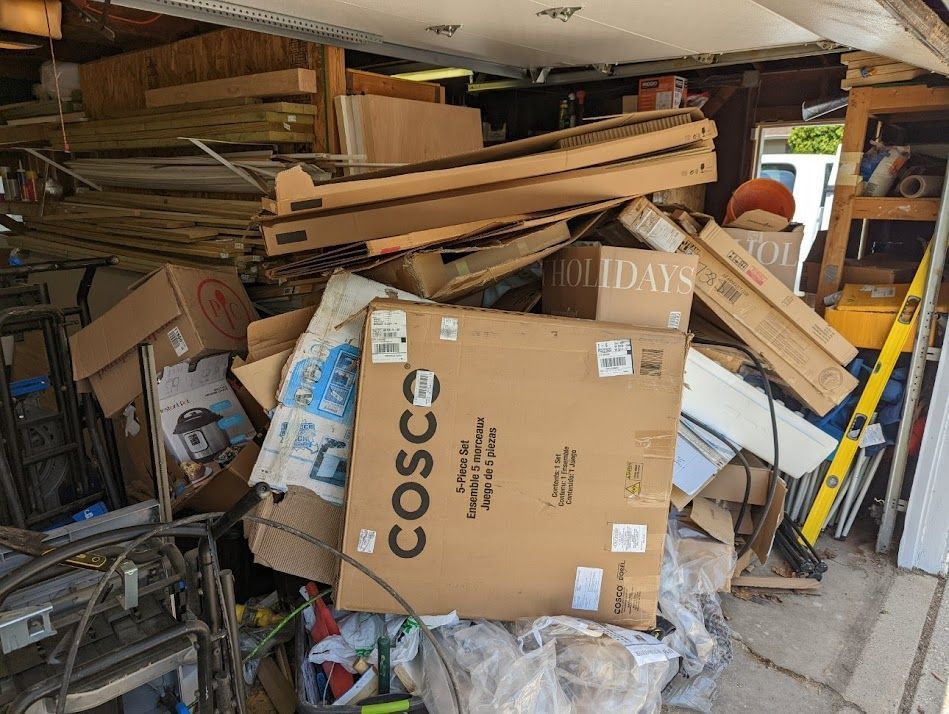 A cluttered garage with a large pile of cardboard boxes and wood. A Cosco box is in the foreground.