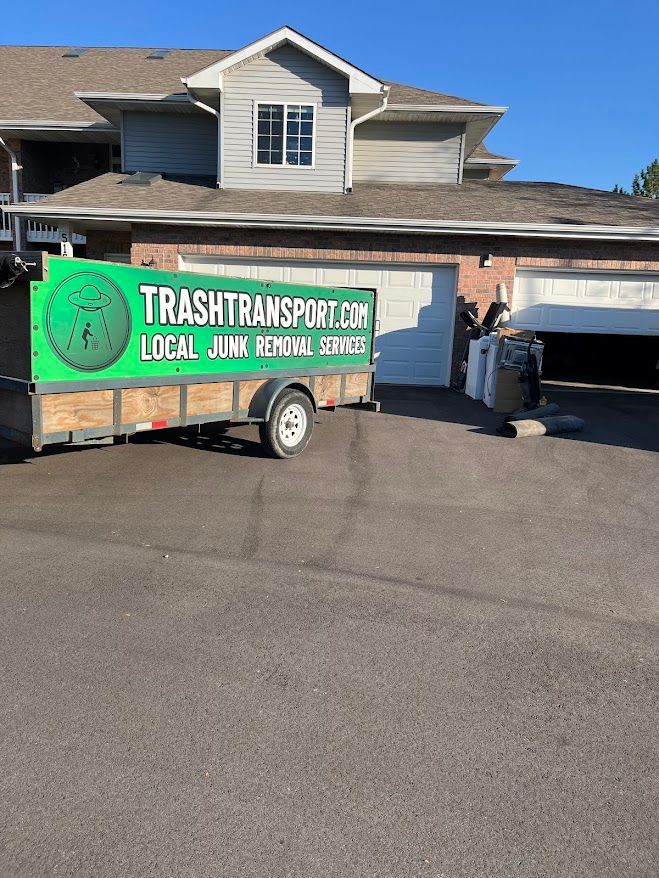 A trailer from TrashTransport.com in a driveway in front of a house and garage. The trailer has a green sign.