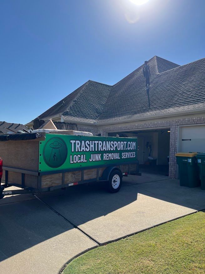 A trailer with the TrashTransport.com logo parked in front of a house on a sunny day.