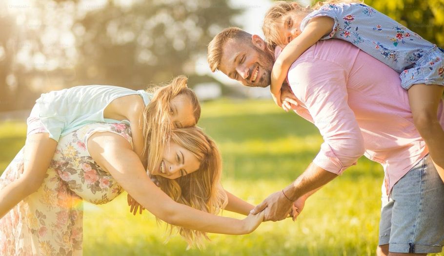 Family playing outdoors, parents giving children piggyback rides on sunny day.