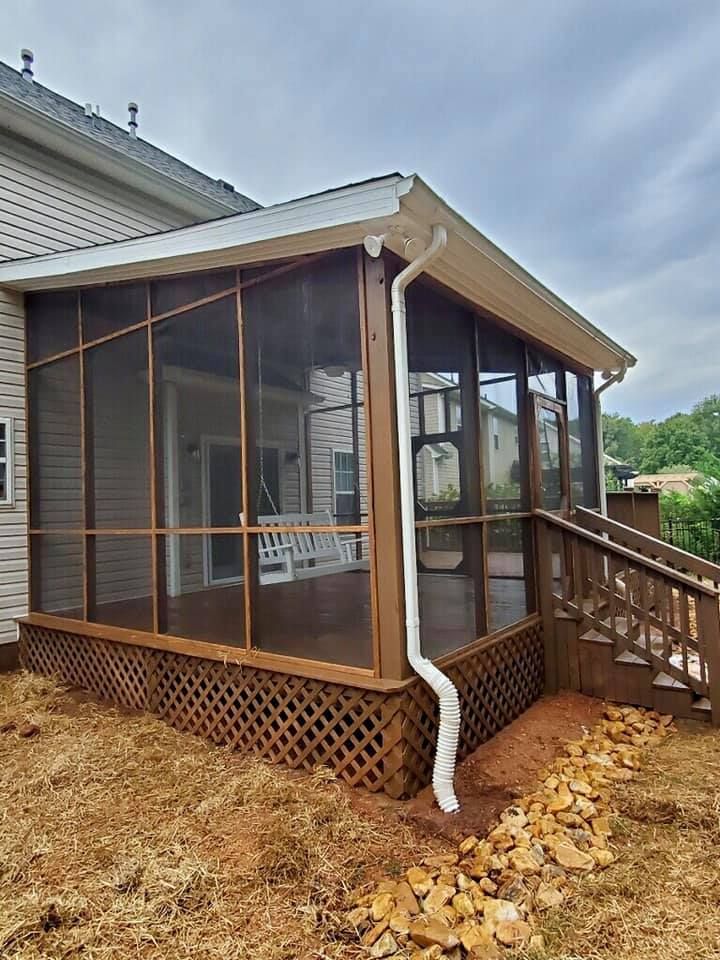 Screened-in porch addition with wood lattice, stairs, and a white downspout beside a house