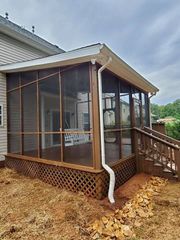Screened porch addition with wooden stairs and lattice skirting beside a house