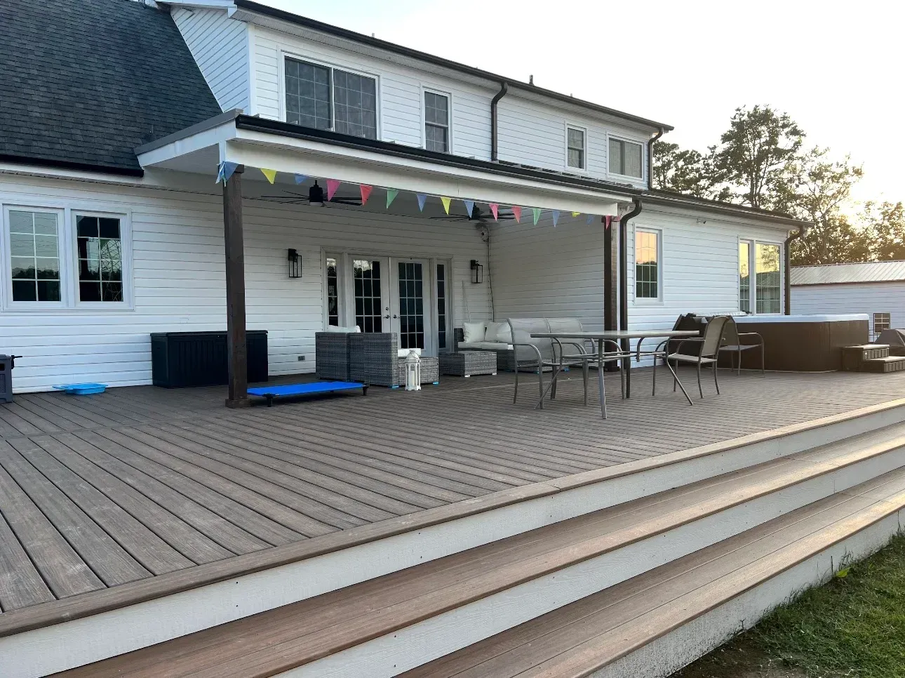 Back deck with white house exterior, covered porch, patio table, and steps leading to the yard