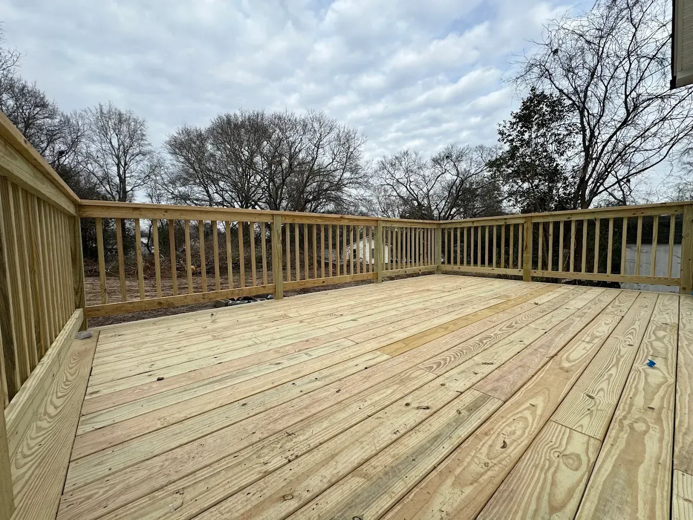 Wooden deck with railings under a cloudy sky, viewed from one corner.