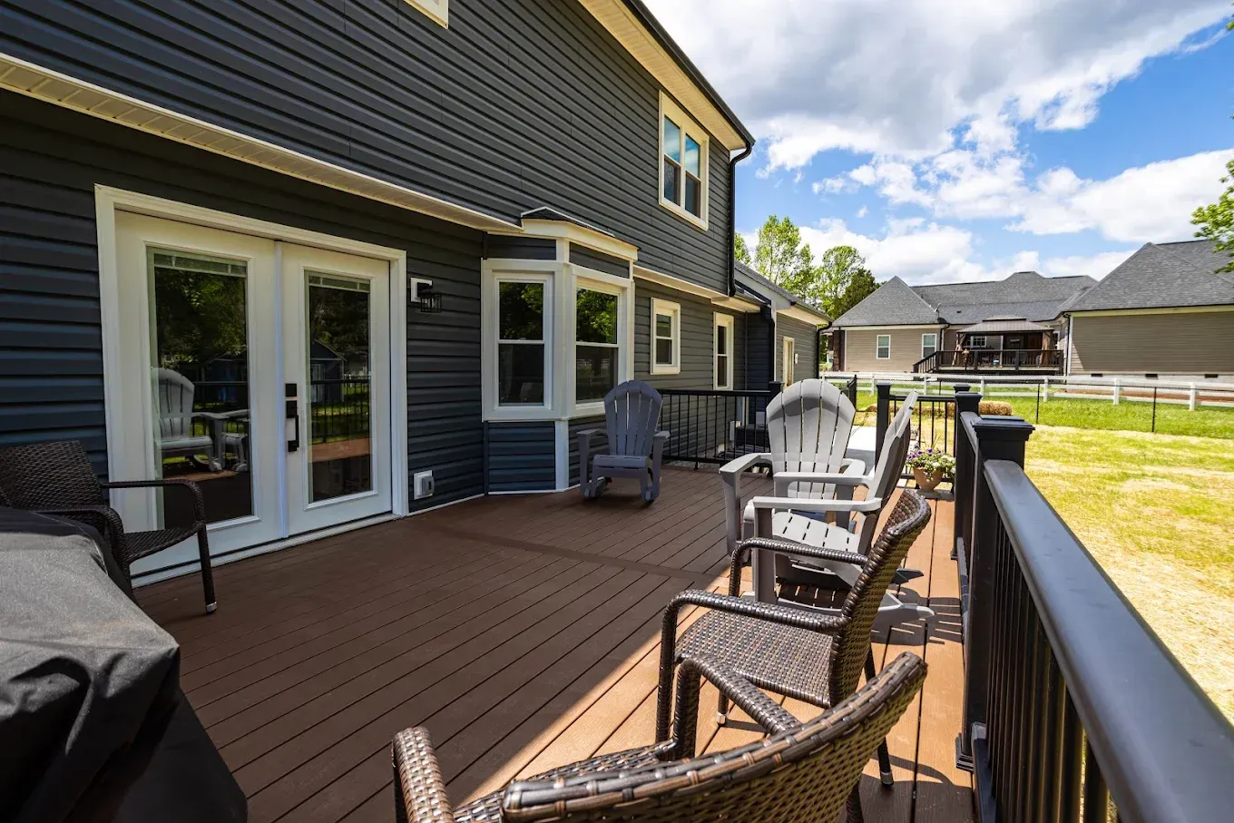 Back deck with outdoor chairs, grill, and sliding glass doors on a house, overlooking a neighborhood and yard