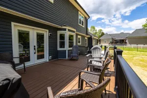 Patio deck beside a dark house with sliding glass doors, wicker chairs, grill, and a view of neighboring homes.