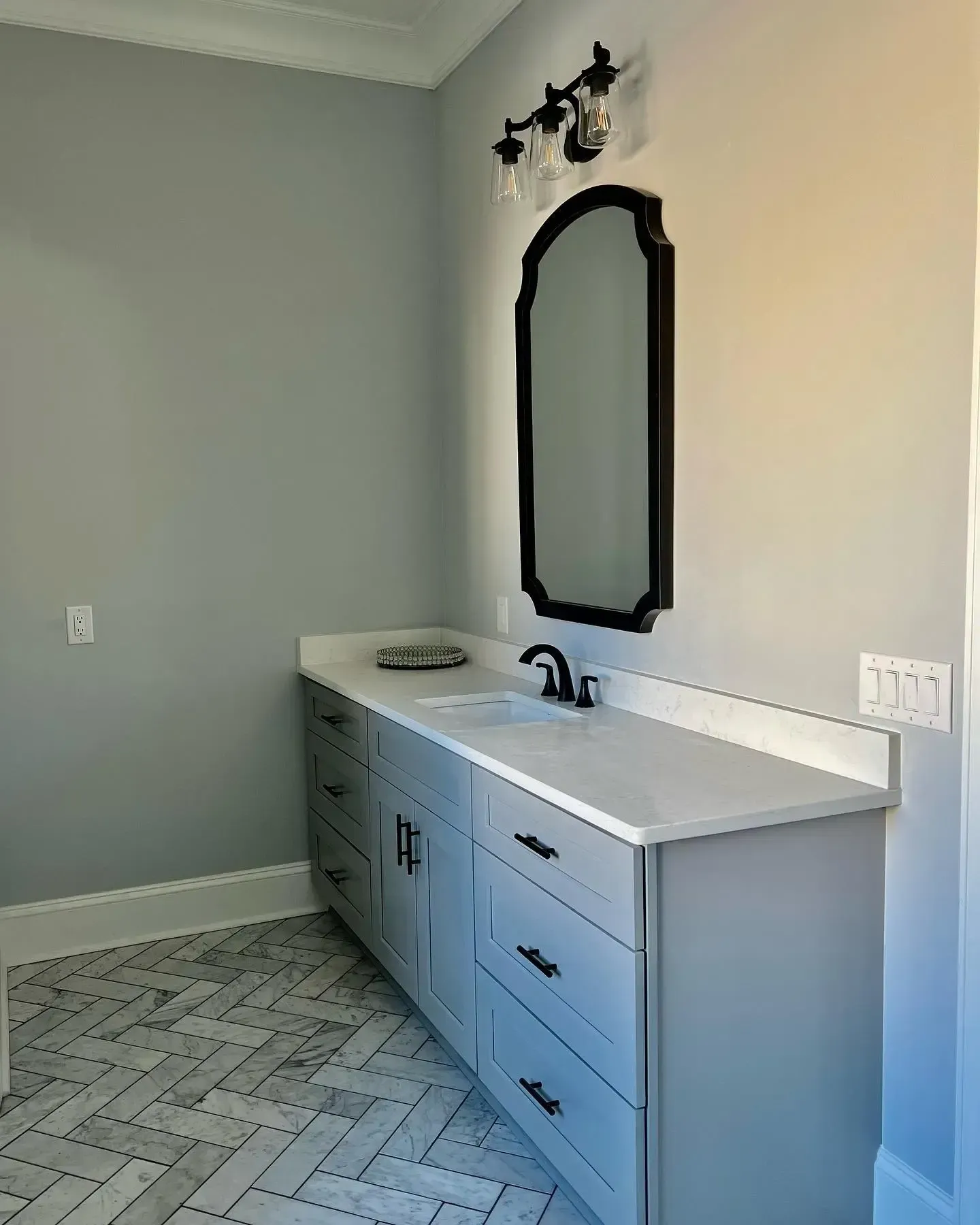 Modern bathroom vanity with white countertop, black-framed mirror, and gray walls and floor tiles