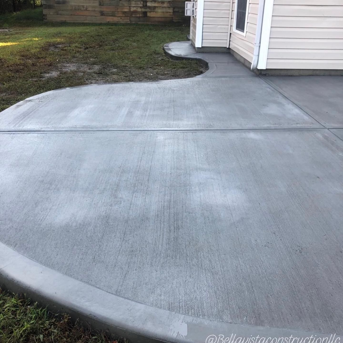 Curved concrete driveway beside a white house and garage corner, bordered by grass.